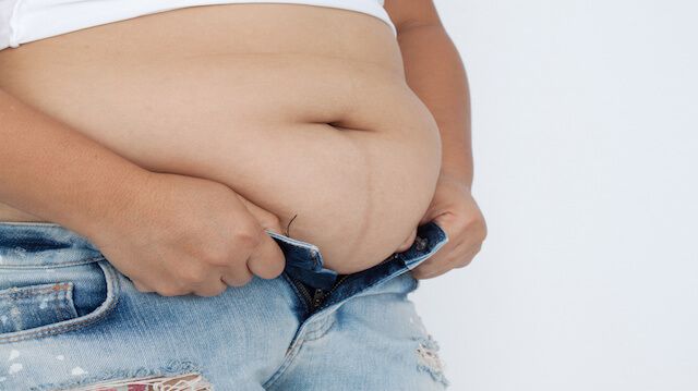 Woman's fingers measuring her belly fat