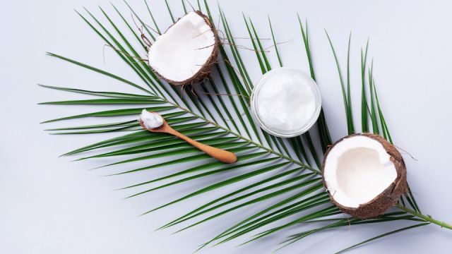 Coconut oil and ripe coconuts, tropical palm and monstera leaves on grey background with copy space. Top view. Summer creative layout.