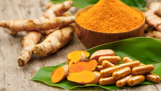 Turmeric powder in wooden bowls and turmeric capsules on wooden background